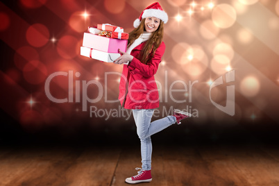 Composite image of festive redhead holding pile of gifts