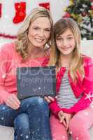 Composite image of festive mother and daughter showing tablet screen