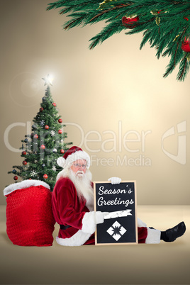 Composite image of santa sits leaned on his bag with a board