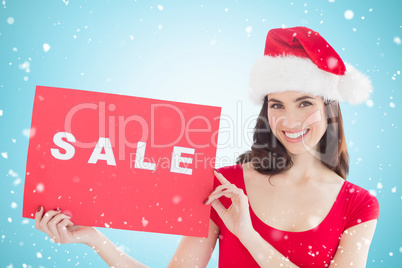 Composite image of festive brunette with sale sign