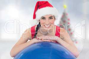 Composite image of festive fit brunette leaning on exercise ball