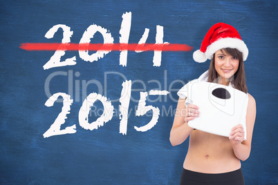 Composite image of festive fit brunette holding a weighing scale