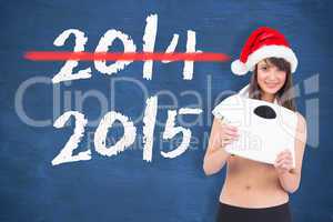 Composite image of festive fit brunette holding a weighing scale