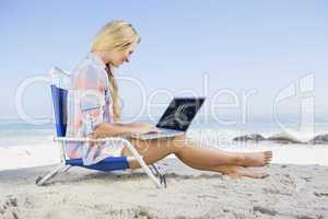 Composite image of woman sitting on beach using her laptop