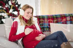 Composite image of pregnant woman rubbing her belly on the couch