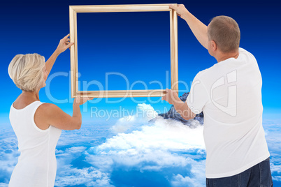 Composite image of mature couple hanging up picture frame