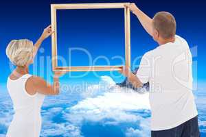 Composite image of mature couple hanging up picture frame