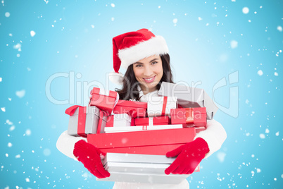 Composite image of smiling brunette in santa hat holding stack o