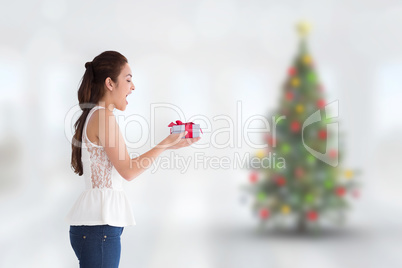 Composite image of surprised brunette holding a present