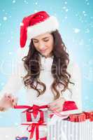 Composite image of happy brunette in santa hat packing gifts