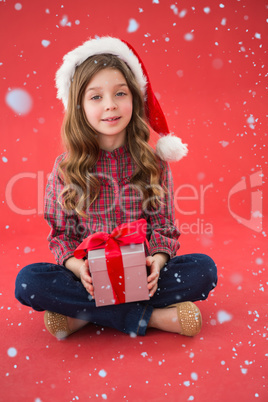 Composite image of happy little girl in santa hat holding gift