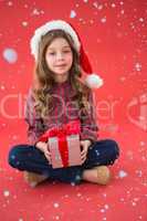 Composite image of happy little girl in santa hat holding gift