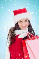 Composite image of cheerful brunette in winter wear holding shop