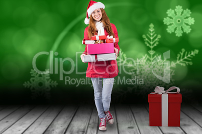 Composite image of festive redhead holding pile of gifts