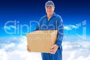 Composite image of happy delivery man holding cardboard box