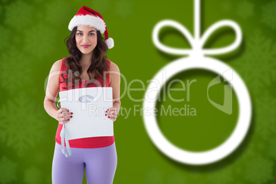 Composite image of festive fit brunette holding page and measuri