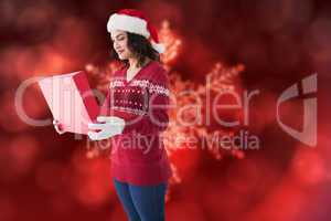 Composite image of festive brunette in winter clothes opening gi