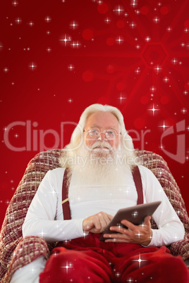 Composite image of smiling santa using tablet on the armchair