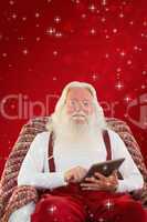 Composite image of smiling santa using tablet on the armchair