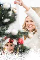 Composite image of festive mother and daughter decorating christmas tree