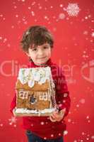 Composite image of festive little boy holding gingerbread house