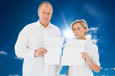 Composite image of upset couple holding torn piece of paper