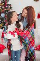 Composite image of festive mother and daughter wrapped in blanket with gifts