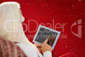 Composite image of rear view of santa using tablet on the armcha