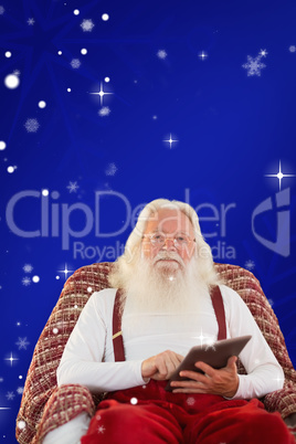 Composite image of smiling santa using tablet on the armchair