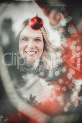 Composite image of festive blonde hanging bauble on christmas tr