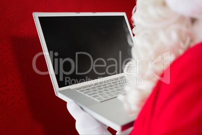 Composite image of father christmas using his laptop