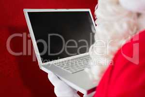 Composite image of father christmas using his laptop