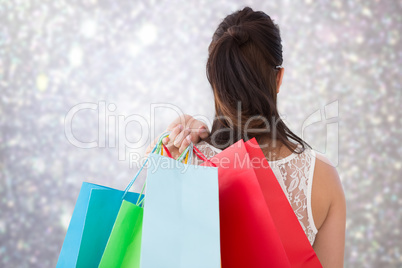 Composite image of rear view of brunette holding shopping bags