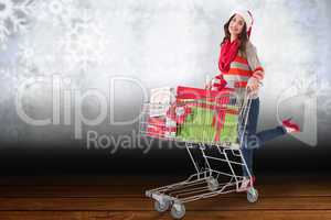 Composite image of festive brunette pushing trolley full of gift