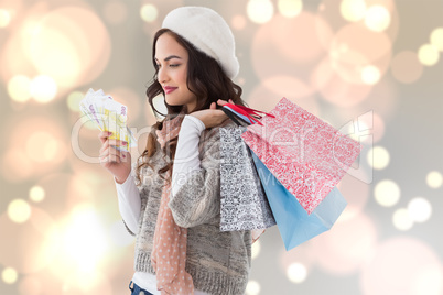 Composite image of happy brunette holding cash and shopping bags