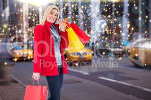 Composite image of happy blonde in winter clothes holding shoppi