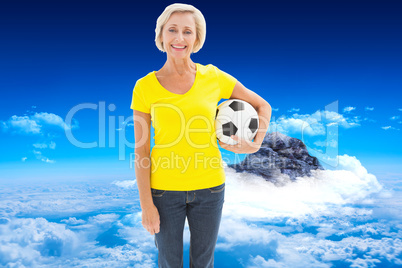 Composite image of mature blonde holding football smiling at cam