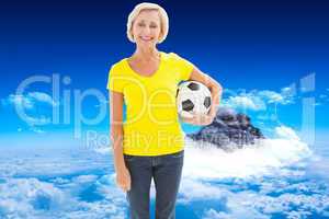 Composite image of mature blonde holding football smiling at cam