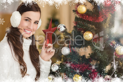 Composite image of smiling brunette holding star near a christma