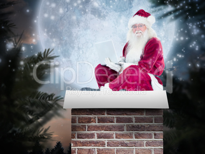 Composite image of santa sits and uses a laptop