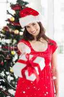 Composite image of festive brunette in red dress holding gift at christmas