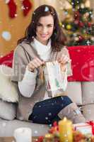 Composite image of brunette opening a gift on the couch at christmas