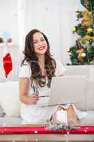 Composite image of smiling brunette shopping online with laptop at christmas