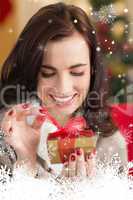 Composite image of smiling brunette opening a gift on christmas day