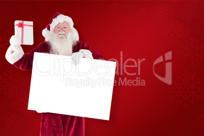 Composite image of santa shows a present while holding sign