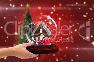 Composite image of hand holding snow globe