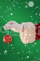 Composite image of santas hand is holding a christmas bulb