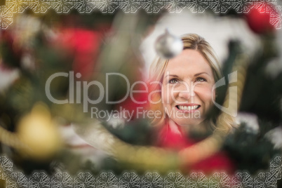 Composite image of festive blonde hanging bauble on christmas tr