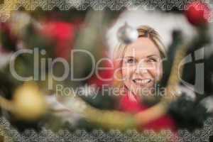 Composite image of festive blonde hanging bauble on christmas tr