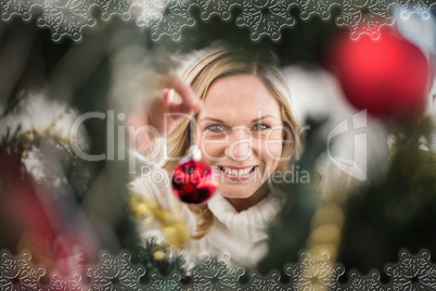 Composite image of festive blonde hanging bauble on christmas tr